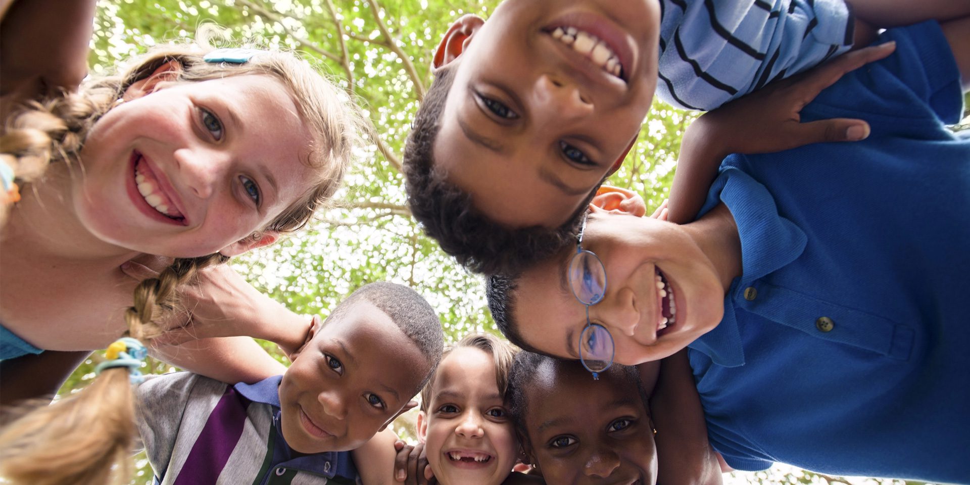 A group of six diverse children smiling in a circle looking down at the camera.