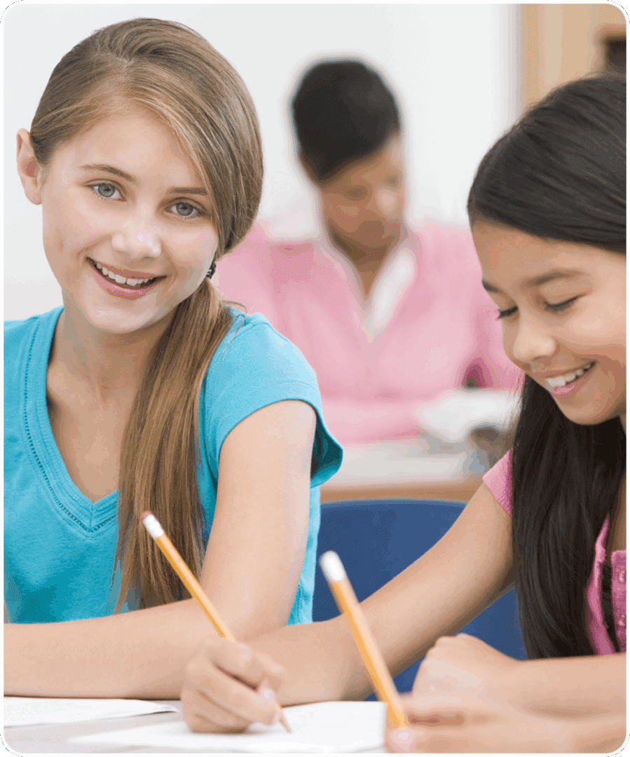 68 Two girls smiling and writing in a classroom.