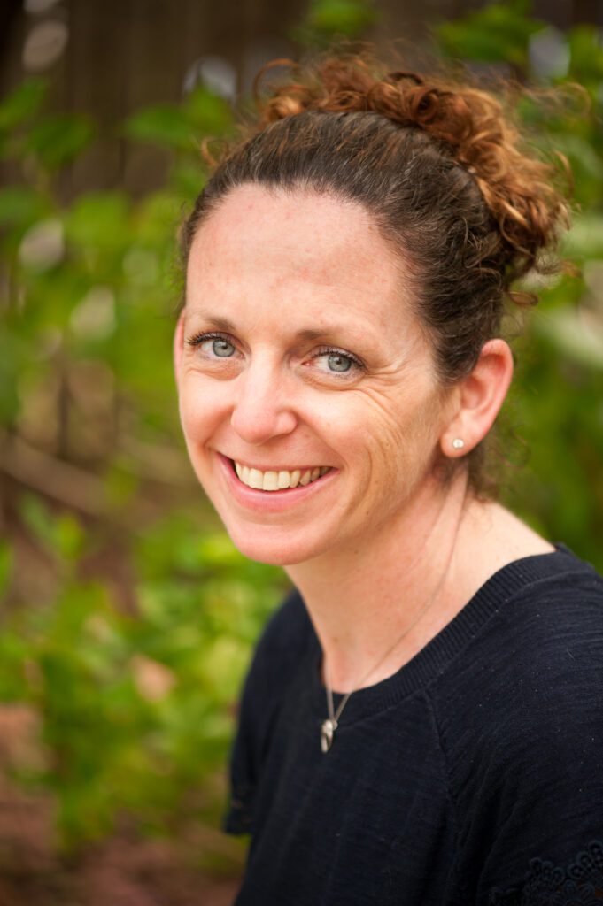 A smiling woman with curly brown hair outdoors.